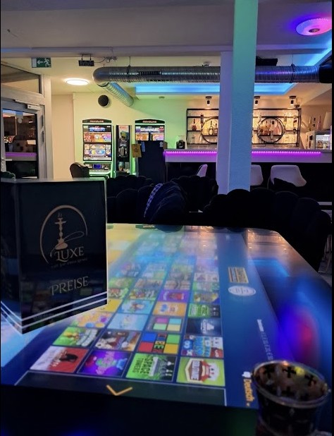Digitaler Spieletisch mit Games-Auswahl in der Luxe Shisha Lounge, im Hintergrund die Neon-Bar